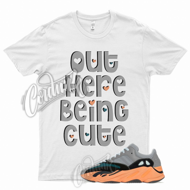 May include: White t-shirt with the text "out here being cute" in gray with small hearts around the text. A pair of gray, black, and orange sneakers are below the shirt.