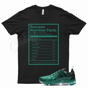 May include: Black t-shirt with a green graphic that reads "Success Nutrition Facts" with a list of qualities needed for success, such as hustle, patience, persistence, ambition, discipline, passion, and grind.  The graphic is in the style of a nutrition facts label.  A pair of green and black sneakers are shown below the t-shirt.