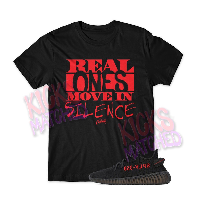 May include: Black t-shirt with red text that reads "REAL ONES MOVE IN SILENCE."  A black and red sneaker is shown below the t-shirt.