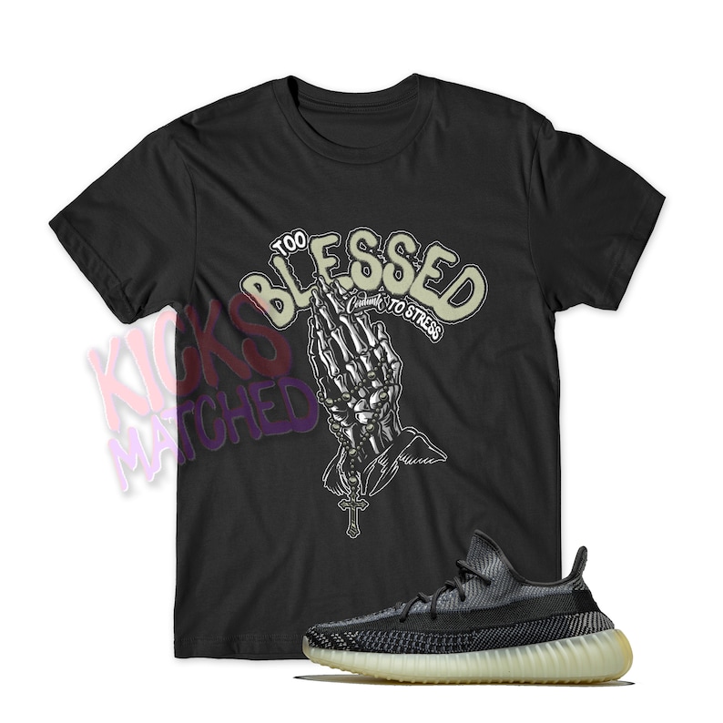 May include: Black t-shirt with a graphic of a praying skeleton hand with the text "Too Blessed to Stress". A pair of black and grey sneakers with a white sole.