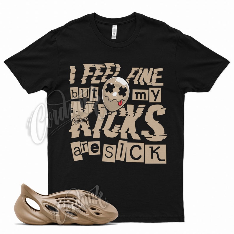 May include: A black t-shirt with a graphic print that says "I feel fine but my kicks are sick". The graphic is in a distressed style with a cartoon balloon face. A pair of tan foam clogs are also pictured.