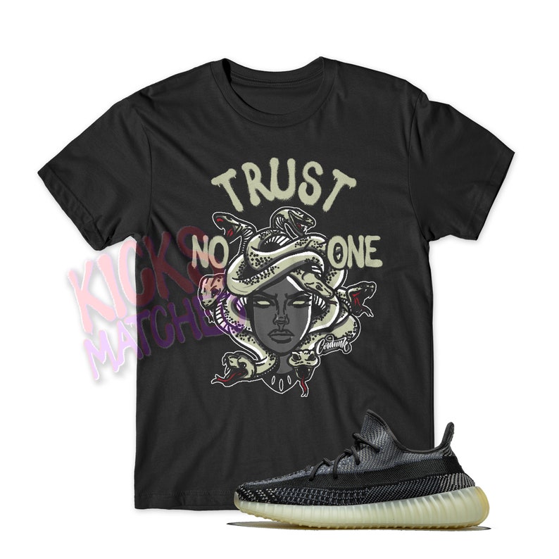 May include: Black t-shirt with a graphic of a woman's face with snakes around her head and the text "TRUST NO ONE". A pair of black and white sneakers with a light brown sole.