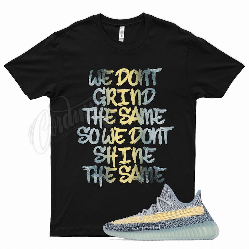 May include: Black t-shirt with the text "We don't grind the same so we don't shine the same" in yellow and blue lettering. A pair of light blue and yellow trainers are shown below the shirt.