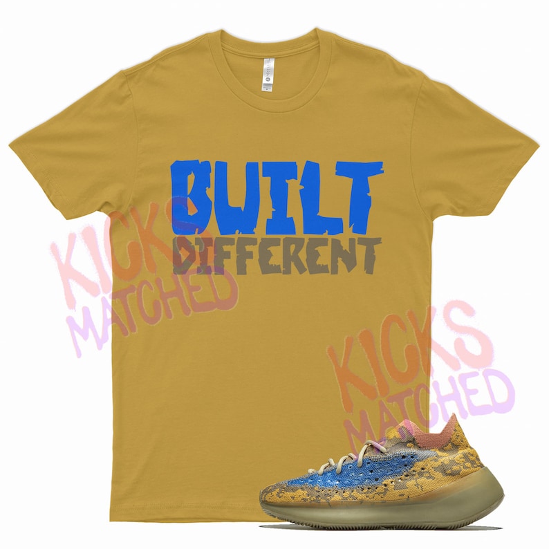 May include: A mustard yellow t-shirt with the text "BUILT DIFFERENT" in blue and gray lettering. A pair of light brown and blue sneakers with a yellow and brown speckled pattern.