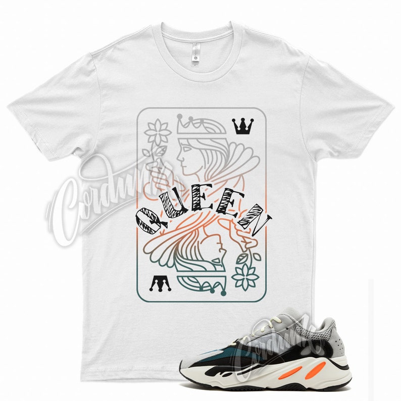 May include: White t-shirt with a graphic of a queen of hearts playing card with the word "QUEEN" printed on it.  A pair of green, black, and white sneakers are shown below the t-shirt.
