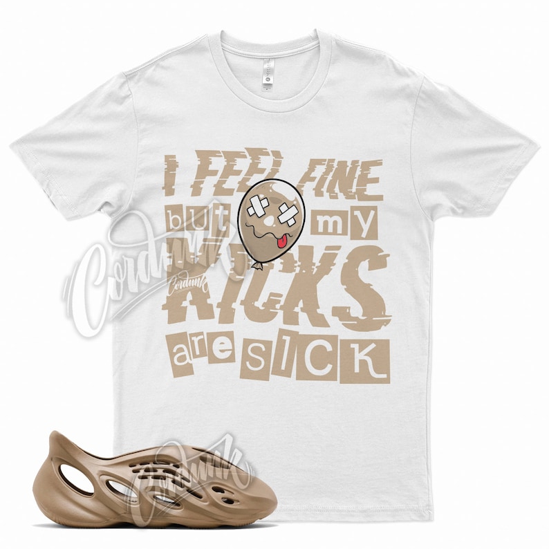 Pode incluir: Camiseta branca com um gr&aacute;fico marrom que diz "I feel fine but my kicks are sick". O gr&aacute;fico apresenta um bal&atilde;o de desenho animado com uma cara triste e bandagens. Um par de tamancos de espuma marrom est&atilde;o na parte inferior da imagem.