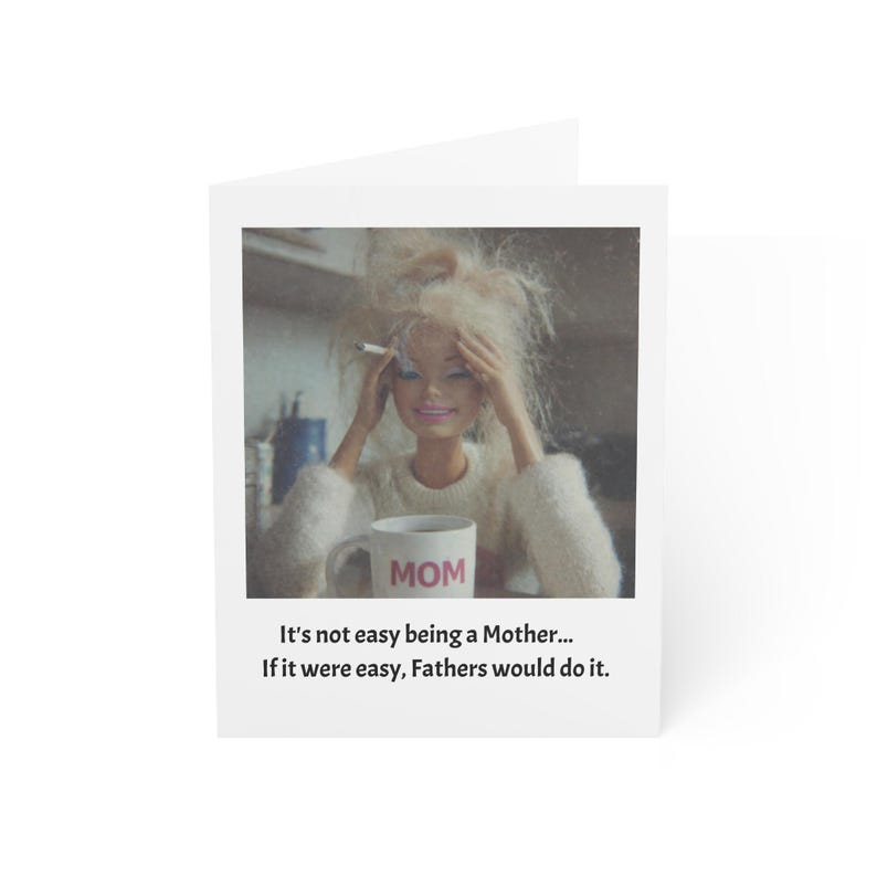 K&ouml;nnte beinhalten: Eine wei&szlig;e Gru&szlig;karte mit einer Puppe mit blonden Haaren, die einen wei&szlig;en Pullover tr&auml;gt und eine Zigarette h&auml;lt. Die Puppe h&auml;lt einen Becher mit der Aufschrift "MOM". Die Karte tr&auml;gt den Text: "Es ist nicht einfach, eine Mutter zu sein... Wenn es einfach w&auml;re, w&uuml;rden V&auml;ter es tun."