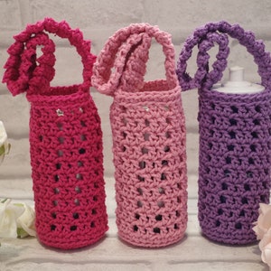 May include: Three crocheted bottle holders in pink, light pink, and purple. Each holder has a crocheted handle and is made with a lacy stitch pattern.