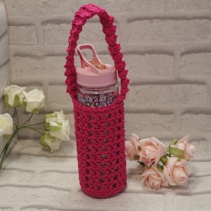 May include: A fuchsia crochet water bottle holder with a matching handle. The holder encases a clear water bottle with a pink lid. The bottle has a floral pattern inside. The background includes white and pink roses.