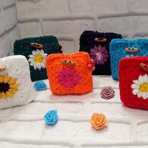 May include: Six crocheted pouches with different floral designs. The pouches are made in various colors, including white, green, orange, blue, and red. Each pouch has a wooden button closure.