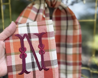 May include: A rectangular fabric piece featuring an autumn plaid pattern in shades of orange, cream, brown, and green. The fabric is embroidered with a large burgundy letter N. Text on the image reads: Autumn Plaid Fabric, Burgundy Letter, Cranberry Knot.