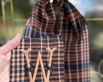May include: A black and copper plaid fabric ribbon featuring a single embroidered monogram letter W in copper thread with black decorative knots. The fabric has a repeating pattern of thin white, copper, and black lines throughout the material.