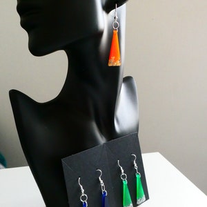 May include: A set of three pairs of dangle earrings. Each pair features a triangular shaped resin pendant with gold glitter embedded in the resin. The pendants are orange, green, and blue.