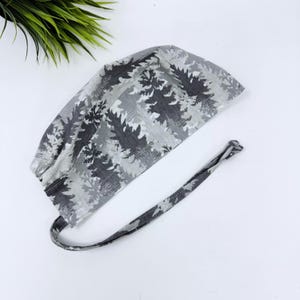 May include: A gray and white patterned scrub cap with a tie closure. The cap features a repeating leaf design in shades of gray. The tie is made of the same fabric and pattern as the cap.