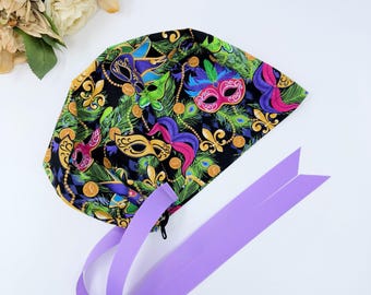 May include: A black scrub hat with a colorful Mardi Gras mask print and purple ties. The hat has a zipper closure.