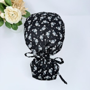 May include: Black scrub hat with a white butterfly print. The hat has a drawstring closure and is made of a soft, comfortable fabric.