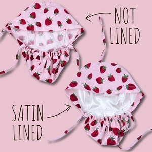 May include: Pink bonnet with a strawberry pattern. The bonnet is shown both satin-lined and not lined. The strawberries are red with green leaves, and the background is a light pink with white polka dots. The bonnet has ties.