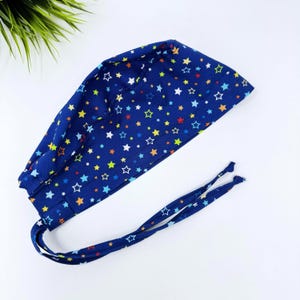 May include: A navy blue surgical scrub cap with a colorful star pattern. The cap has a tie closure and is made of a soft fabric. The stars are in various colors, including red, yellow, and blue.
