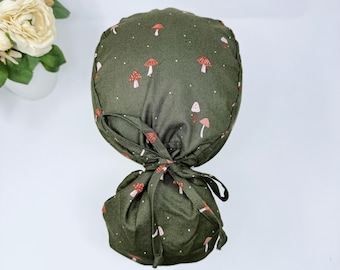 May include: A green scrub hat with a white and red mushroom print. The hat has a tie at the back.
