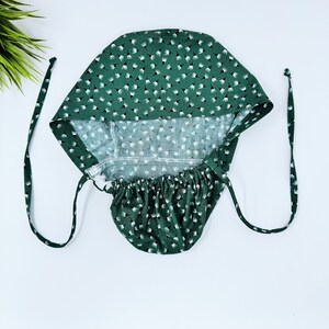 May include: A green fabric hat with a white floral pattern. The hat has a gathered elastic band at the bottom and ties at the top.