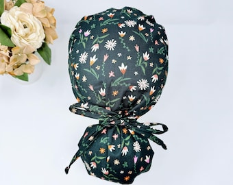 May include: A dark green scrub hat with a floral print featuring white, pink, and orange flowers. The hat has a tie at the back.