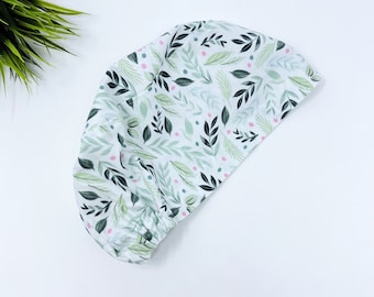May include: A white scrub cap with a green and pink floral pattern. The cap has a gathered elastic band at the bottom.
