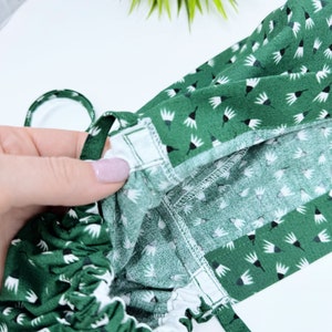 May include: Close-up of a green fabric with a white floral pattern. The fabric is gathered at the top and has a white elastic band.