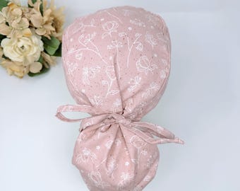 May include: A pink scrub hat with a white floral pattern. The hat has a tie at the back.