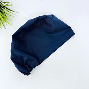 May include: A navy blue surgical scrub cap made from a soft, durable fabric. The cap is designed to cover the hair and is commonly used in medical settings. The cap is a solid colour and has a simple, functional design.