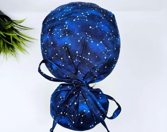May include: A dark blue scrub cap with a celestial constellation pattern. The cap features white star constellations against a dark blue background, with a matching tie closure at the back. The cap is designed for medical professionals.