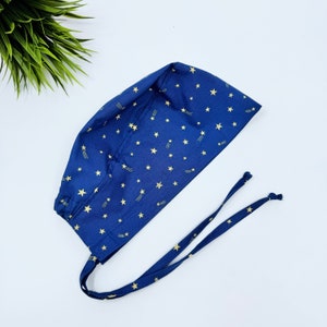 May include: A blue surgical scrub hat with a gold star and shooting star pattern. The hat has a tie that can be adjusted to fit.