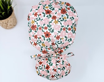 May include: A white scrub cap with a floral print featuring pink, red, and green flowers. The cap has a tie at the back.