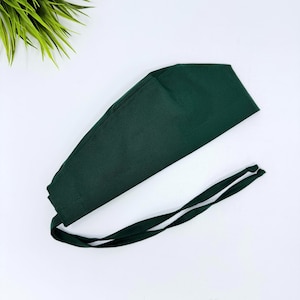May include: A dark green scrub cap with long ties. The cap is made of a solid, opaque fabric and is designed to cover the hair during medical procedures. The ties are white with a dark green border.