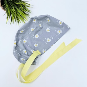 May include: A gray scrub hat with a white daisy print and yellow ties.