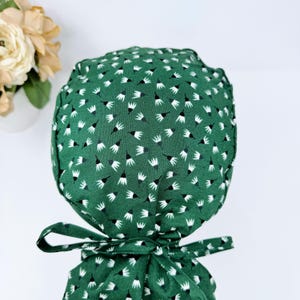May include: A green scrub hat with a white and black patterned design. The hat has a tie on the back.