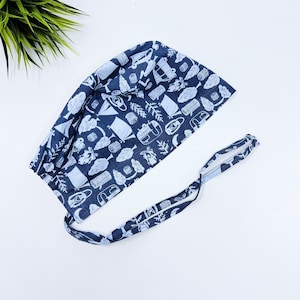 May include: A blue and white patterned surgical scrub hat with a tie. The pattern features camping and outdoor themed illustrations.