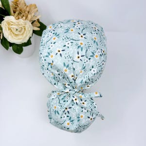 May include: A light blue scrub hat with a white and yellow floral pattern. The hat has a tie at the back.