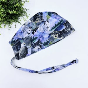 May include: A blue and white surgical scrub hat with a wolf and eagle print. The hat has a tie that can be tied at the back of the head.