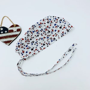 May include: White surgical scrub cap with a red, white, and blue star pattern. The cap has two long ties.