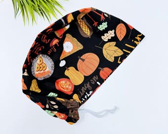 May include: Black scrub hat with a Thanksgiving theme. It features pumpkins, leaves, pie, and the text "Fill me with my fall in the air".