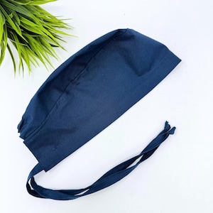 Op de afbeelding: Een marineblauwe chirurgische scrubcap met een striksluiting. De cap is gemaakt van een effen, donkerblauwe stof en is ontworpen om het haar te bedekken tijdens medische procedures. De striksluiting zorgt voor een verstelbare en veilige pasvorm.