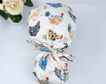 May include: A white scrub hat with a colorful chicken print. The hat has a tie at the back.