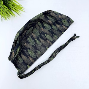 May include: A black scrub cap with a forest pattern featuring green and brown trees. The cap has a tie in the back for an adjustable fit. The fabric is soft and flexible, suitable for medical professionals or anyone needing head covering.