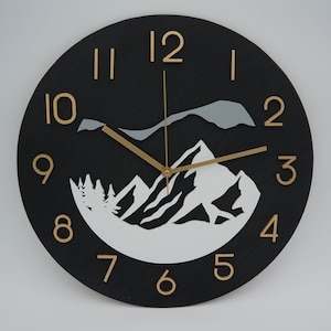 May include: A round black wall clock with gold-colored numerals and hands. The clock face features a mountain scene in white and gray. The clock measures approximately 12 inches in diameter.