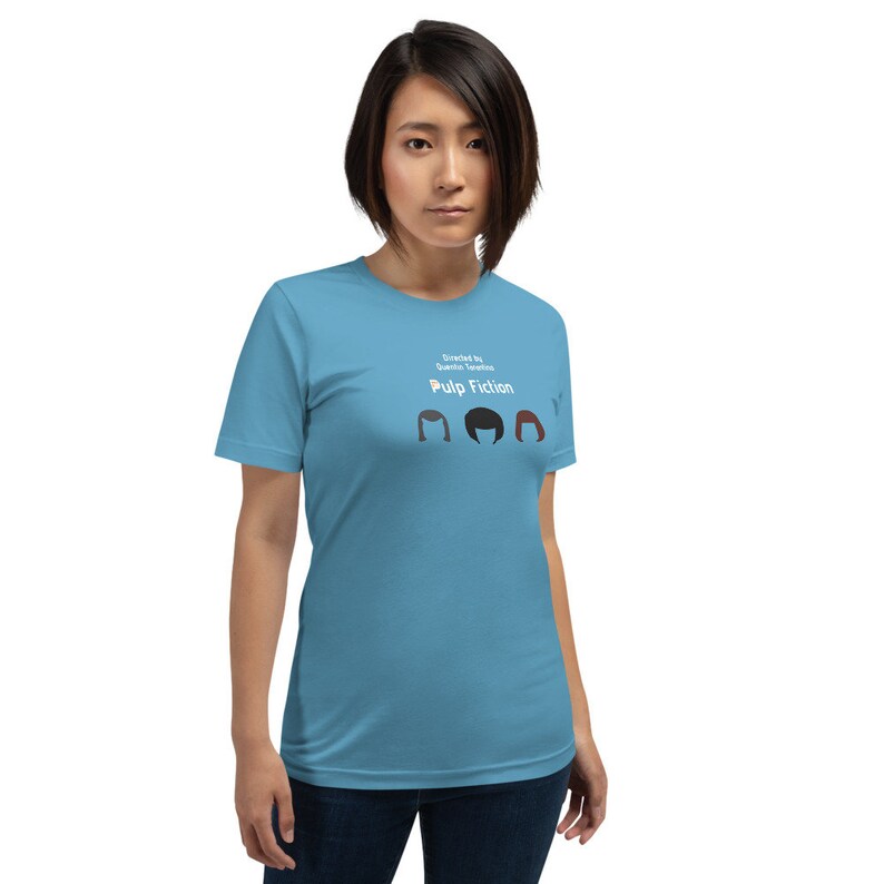 May include: A light blue t-shirt featuring the text "Directed by Quentin Tarantino" and "Pulp Fiction" above three stylized hair silhouettes. The shirt is a solid light blue color.