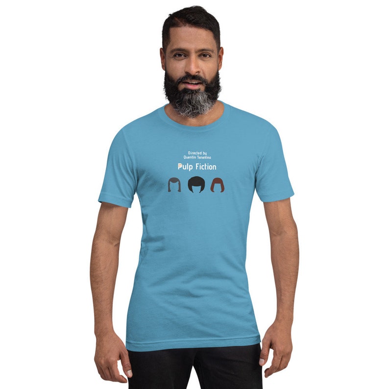 May include: A light blue t-shirt featuring the text "Directed by Quentin Tarantino" and "Pulp Fiction" above three stylized hair silhouettes. The shirt is a solid color and has short sleeves.