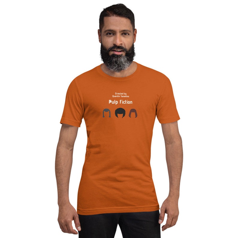 May include: Orange t-shirt with the text "Pulp Fiction" and the words "Directed by Quentin Tarantino" above it. The shirt features three stylized hair silhouettes. The person in the image is wearing the shirt.