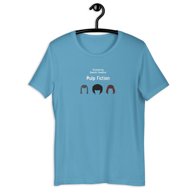 May include: A light blue t-shirt featuring the text "Pulp Fiction" and the phrase "Directed by Quentin Tarantino." Below the text are three stylized hair silhouettes in brown, black, and red.