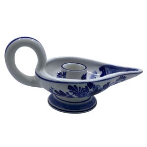 May include: A white ceramic candle holder with a blue floral design. The candle holder has a handle and a spout, and is approximately 15 cm long.