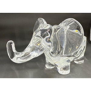 Peut inclure: Une figurine d'éléphant en verre transparent avec une trompe, des oreilles et quatre pattes. L'éléphant est en verre transparent et est posé sur une surface réfléchissante. La figurine est un objet décoratif.